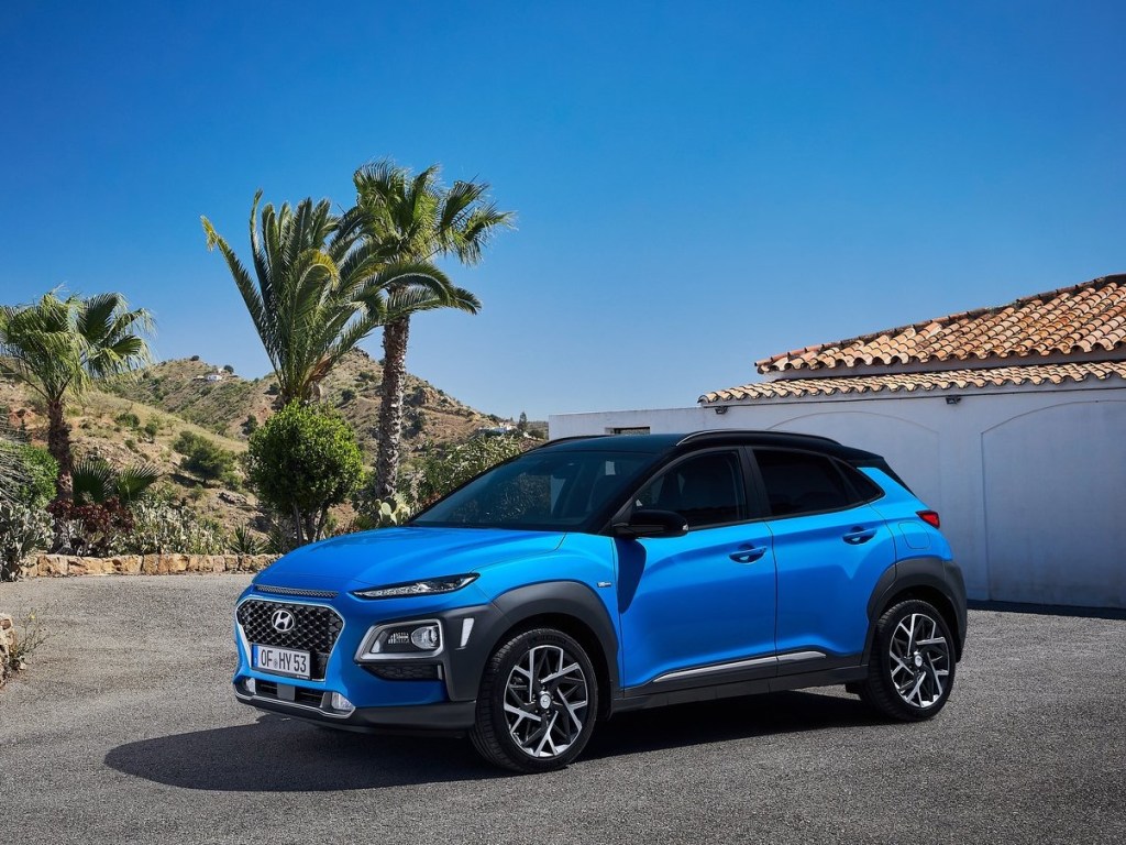 A blue Hyundai Kona Hybrid sits in a driveway lined with palm trees.