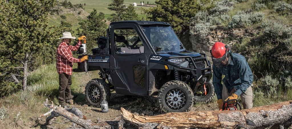 Two lumberjacks work on fallen trees by their side-by-side Ranger XP 1000.