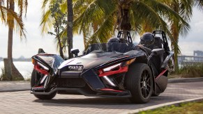 A black-and-red 2020 Polaris Slingshot R in front of a palm-tree-lined marina