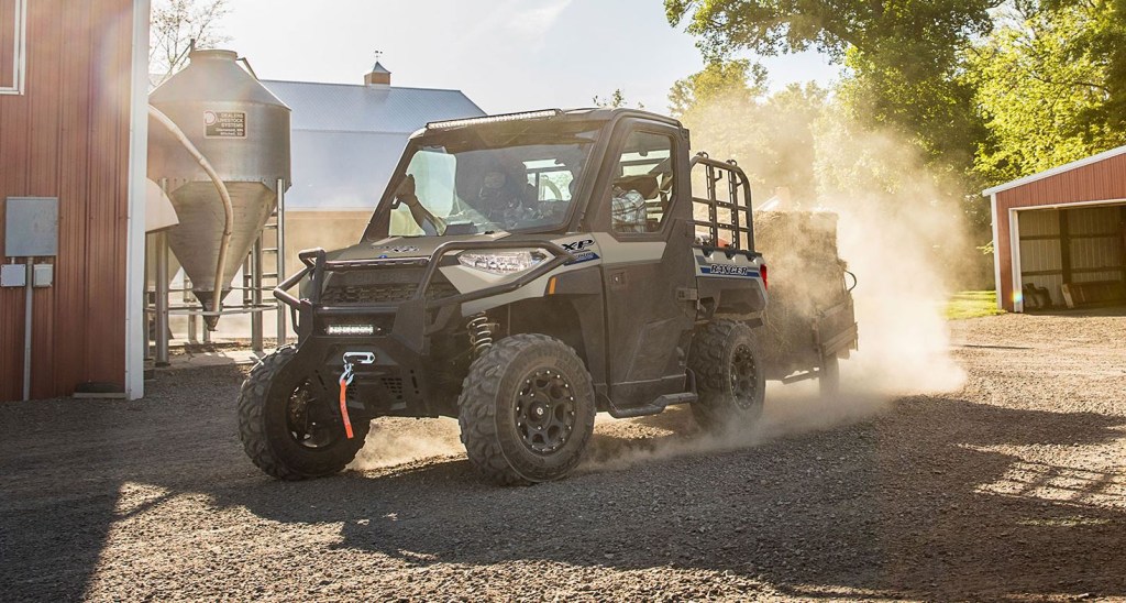 A side-by-side ATV is pulling a small trailer with hay.