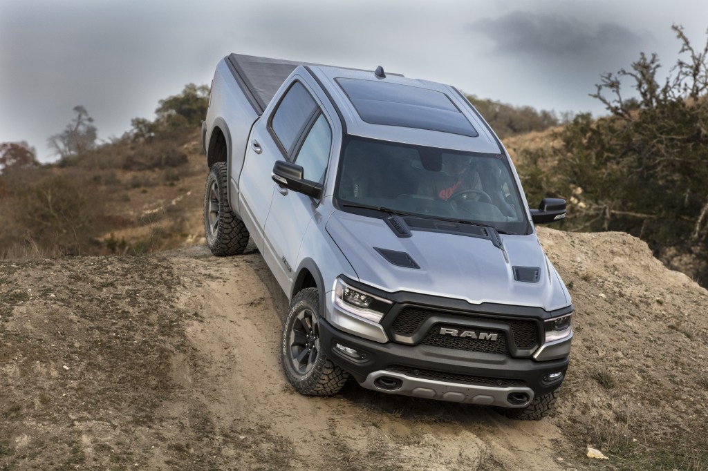 A silver Ram 1500 on a dirt road climbs over the peak of a hill. Ram is part of the FCA family of brands.