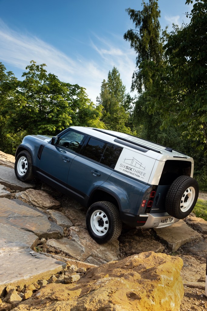 Rear-side view of the 2021 Land Rover Defender Hard Top 110 panel van driving up a rocky hill