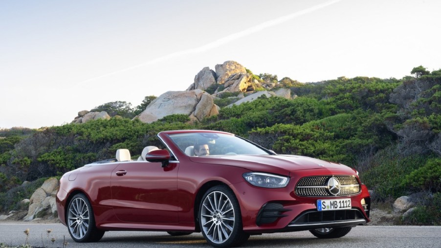 A red 2021 Mercedes E-Class Cabriolet in front of a green-covered rocky hill with its top down