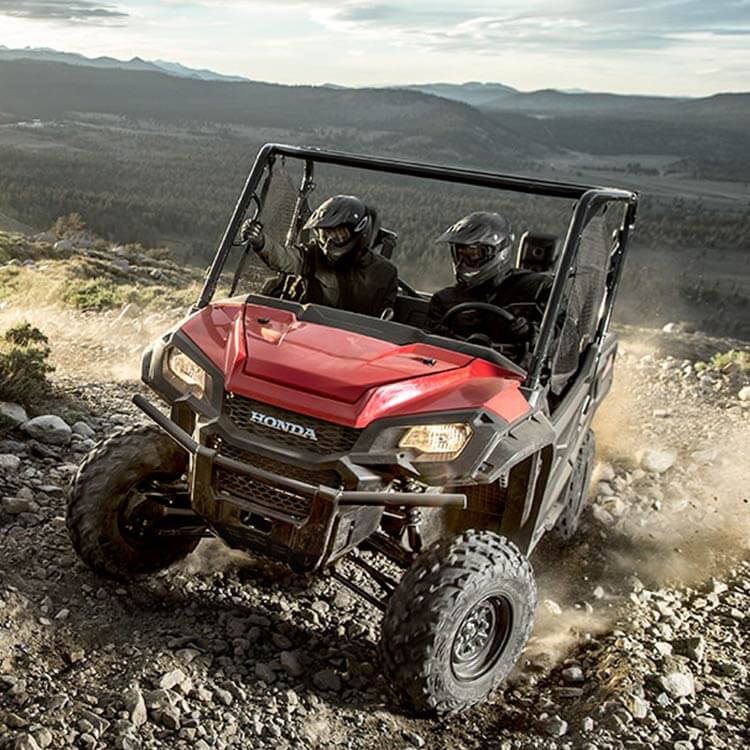 a red Honda Pioneer side-by-side UTV scrambling up a rocky incline. 