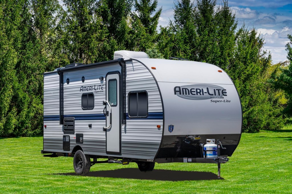 a Gulf Stream Coach RV trailer in a green lawn with a pleasant forested backdrop