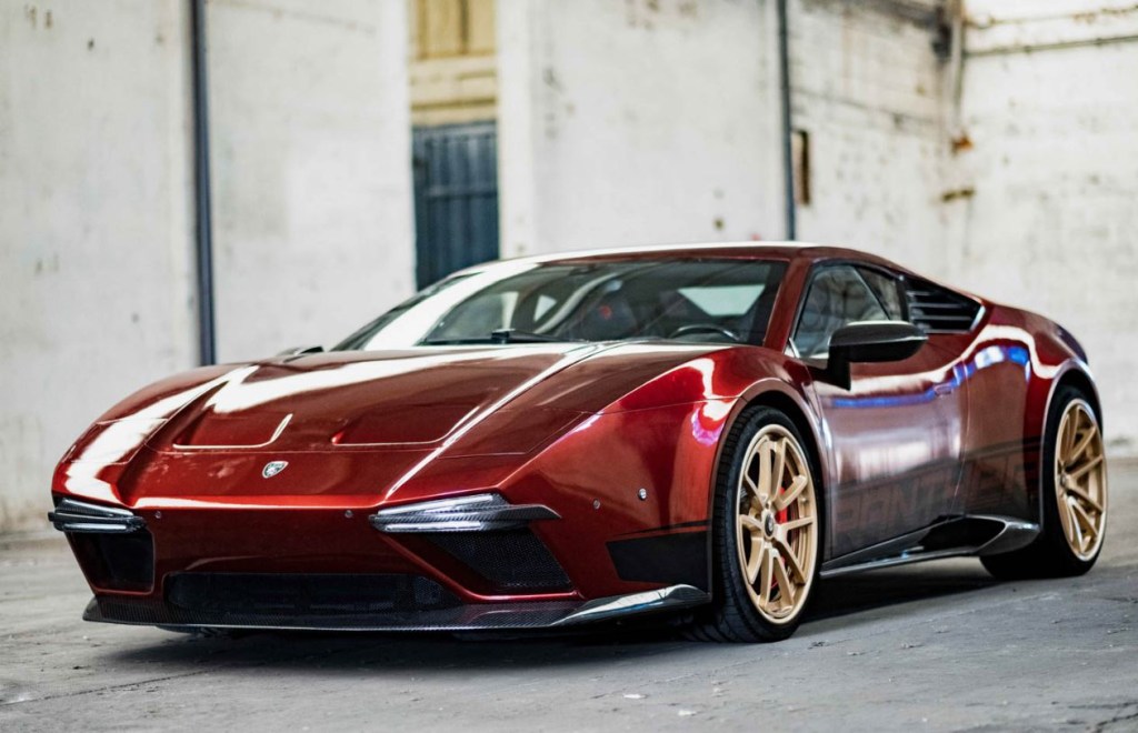 The front of a red Ares Panther is seen as the car sits by a building.