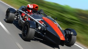 Red Ariel Atom 4 being driven by a helmeted driver down a country road