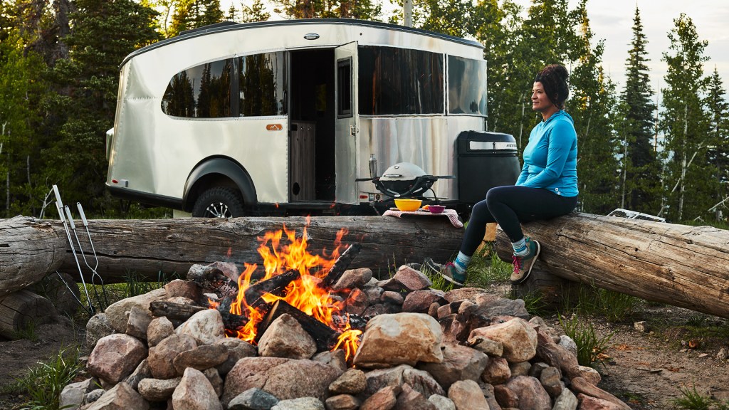 The Airstream Basecamp travel trailer RV is parked by a campfire.