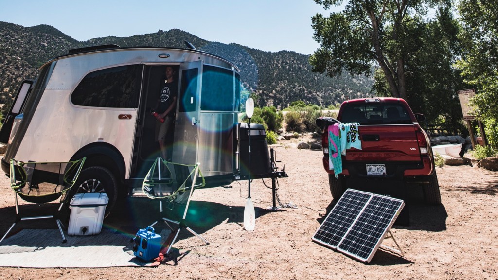 The Airstream travel trailer is by a campsite, a truck, and solar panels.