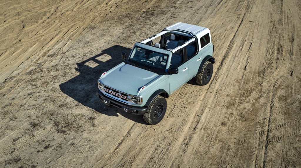 A gray four door bronco is on a dirt road and has its front and mid section tops off.