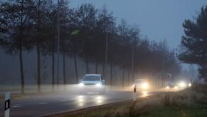 Cars with LED headlights driving on a foggy road.