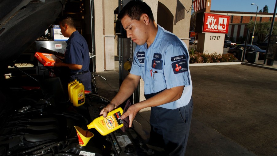 A man pours a new bottle of oil into a car
