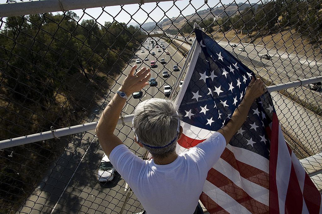 boy waves flag on overpass with freeway below