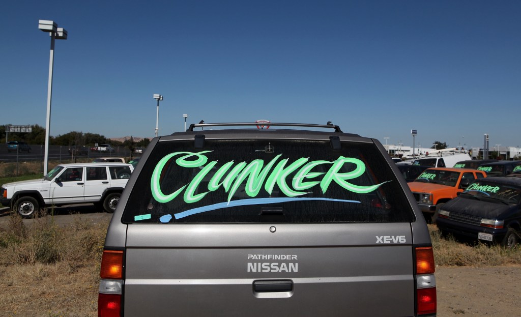 The rear of an old SUV has "Clunker" written across the liftgate glass. 