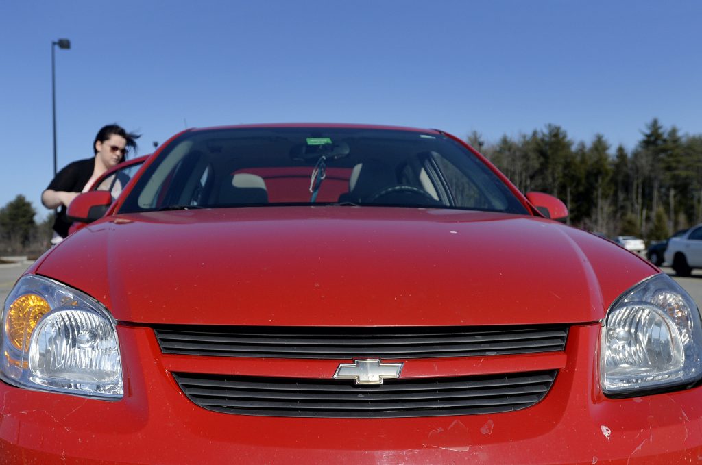 A woman places something in the back of her red Chevy Cobalt.