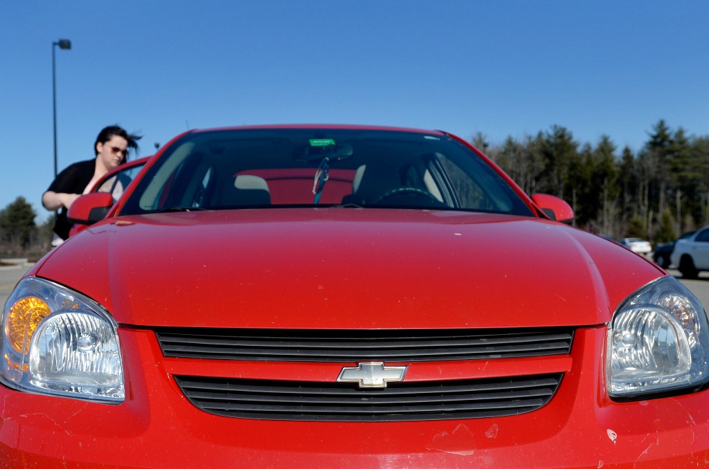 A woman places something in the back of her red Chevy Cobalt.