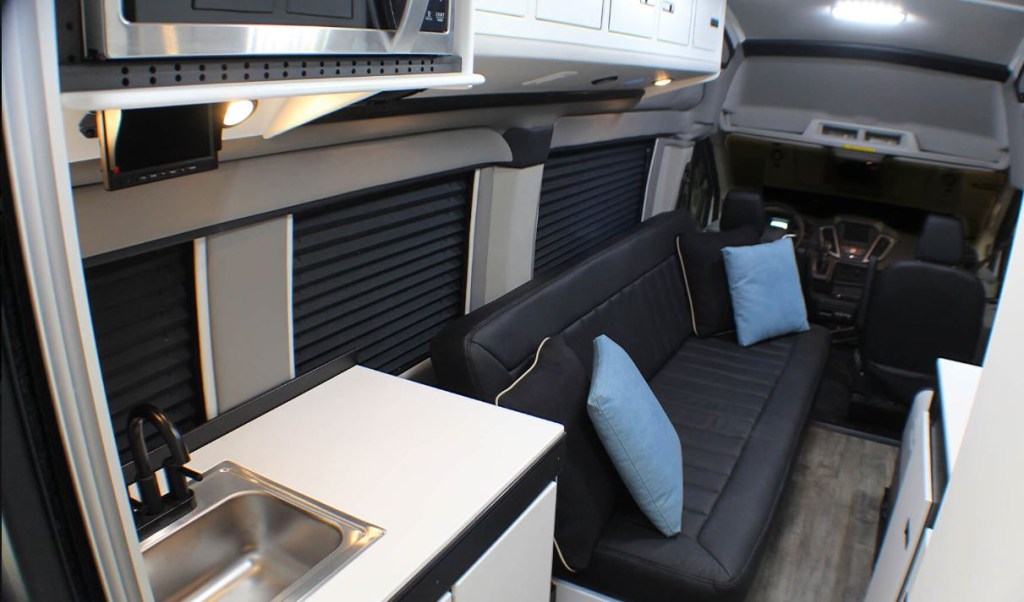 The interior of the RV has a black sofa and a small kitchen.