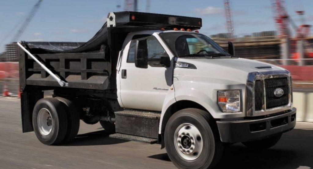 A white F-750 dump truck on a roadway near a construction site.