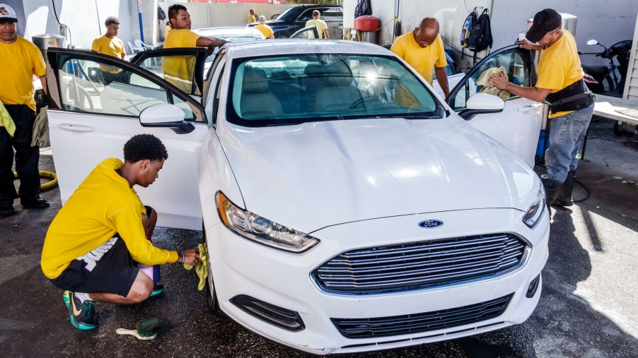 A white Ford Fusion at a car wash with several workers carefully polishing it
