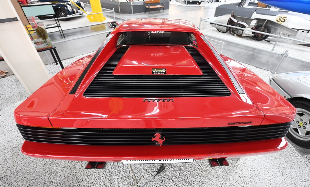 The rear of a red Ferrari Testarossa that is on display at a museum