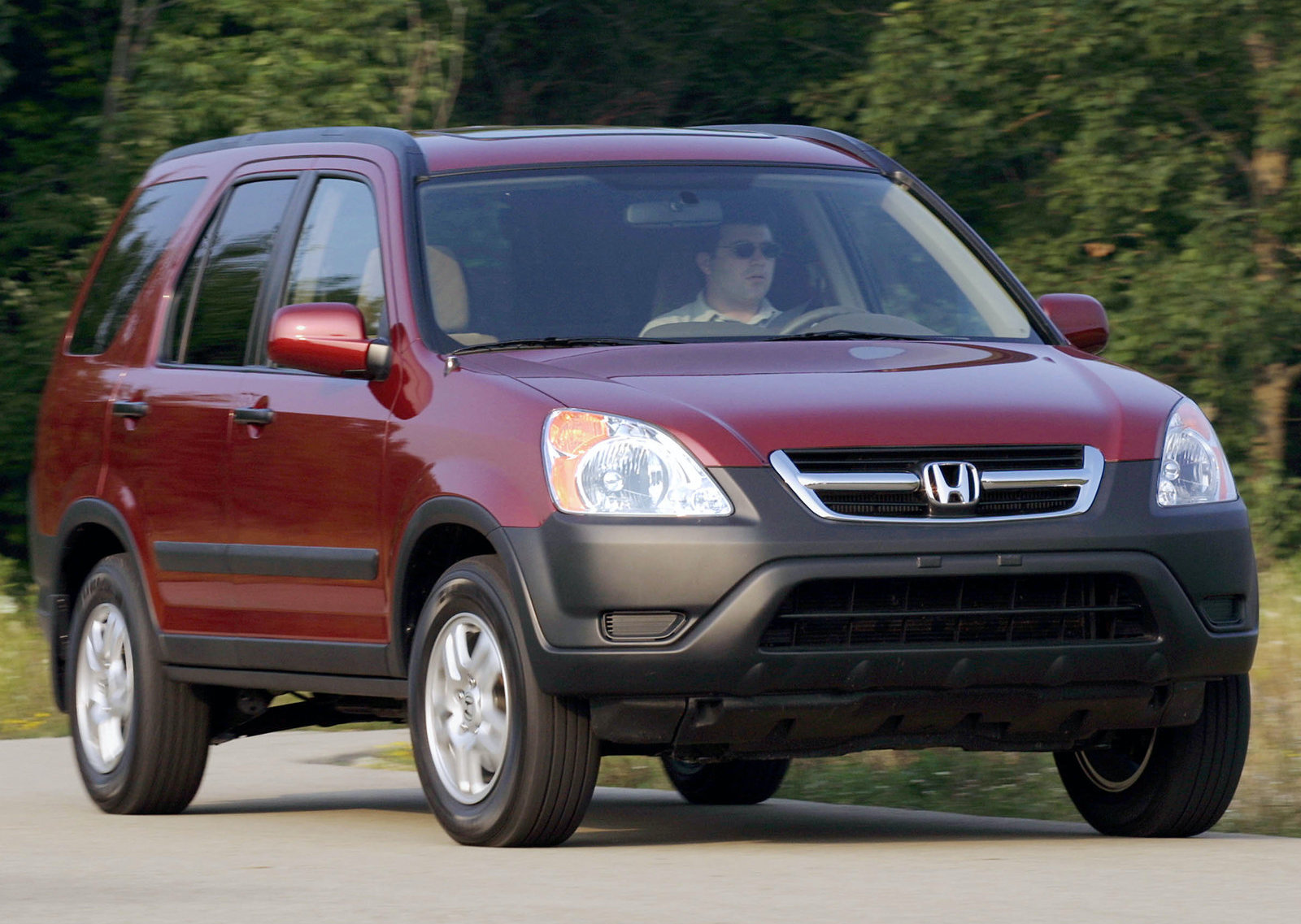 a maroon used Honda CR-V driving on a scenic treed road. 