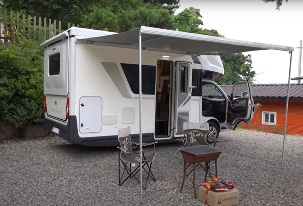 A campsite is set up under the canopy attached to a white Hyundai Porest RV.