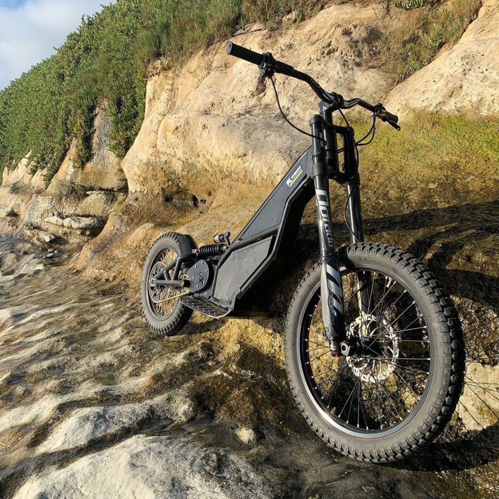 A black Kuberg Ranger Standard propped up on a rocky lakeshore