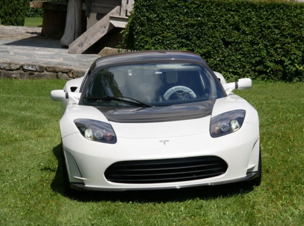 A white Tesla Roadster sits on grass in a yard.