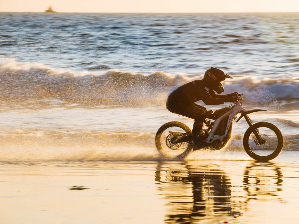 A rider on the beach racing the waves on the white electric Segway eBike.
