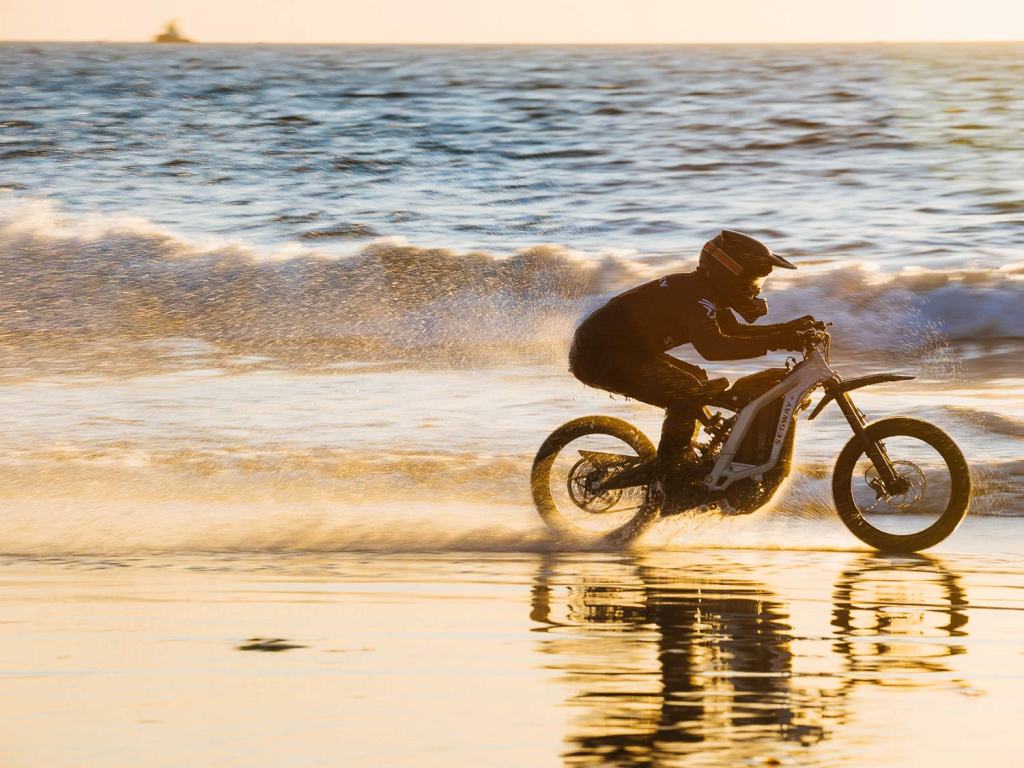 A rider on the beach racing the waves on the white electric Segway eBike.