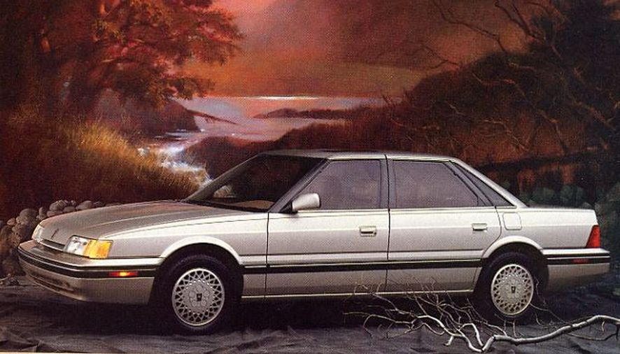 A silver, four door British Sterling sedan sits in a dusk setting. 