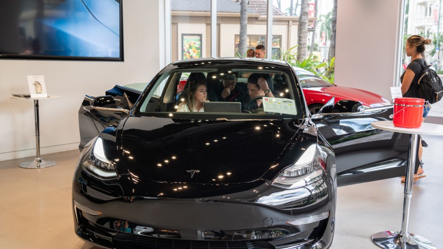 Customers admire a Tesla Model 3 electric vehicle at a Tesla store