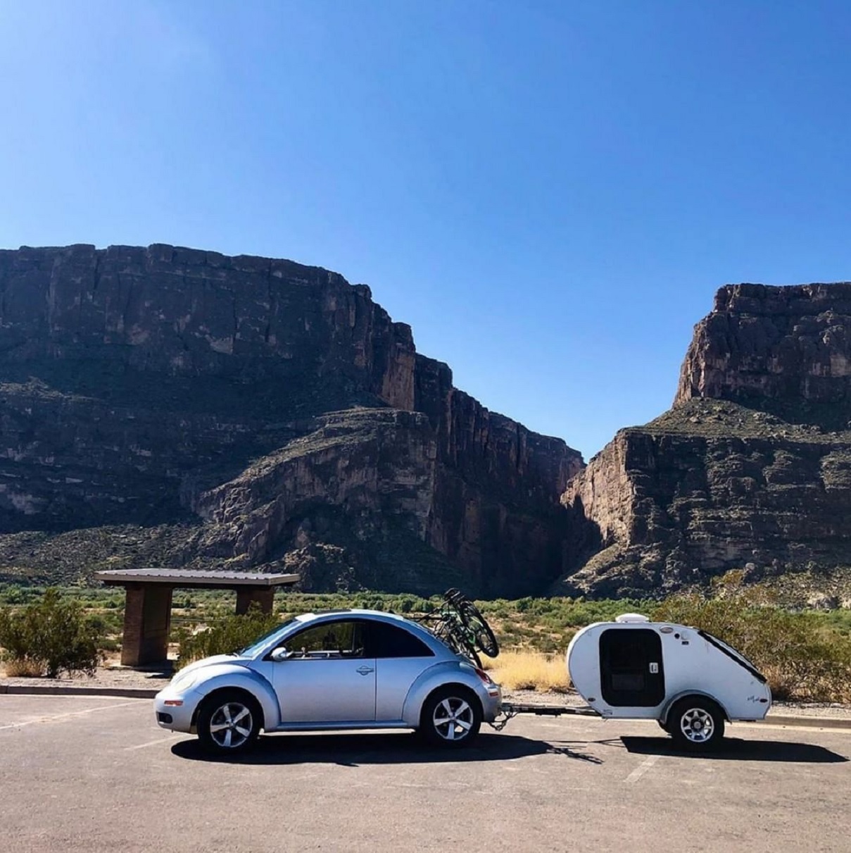 A silver Volkswagen New Beetle towing a trailer, parked in front of a mountain range