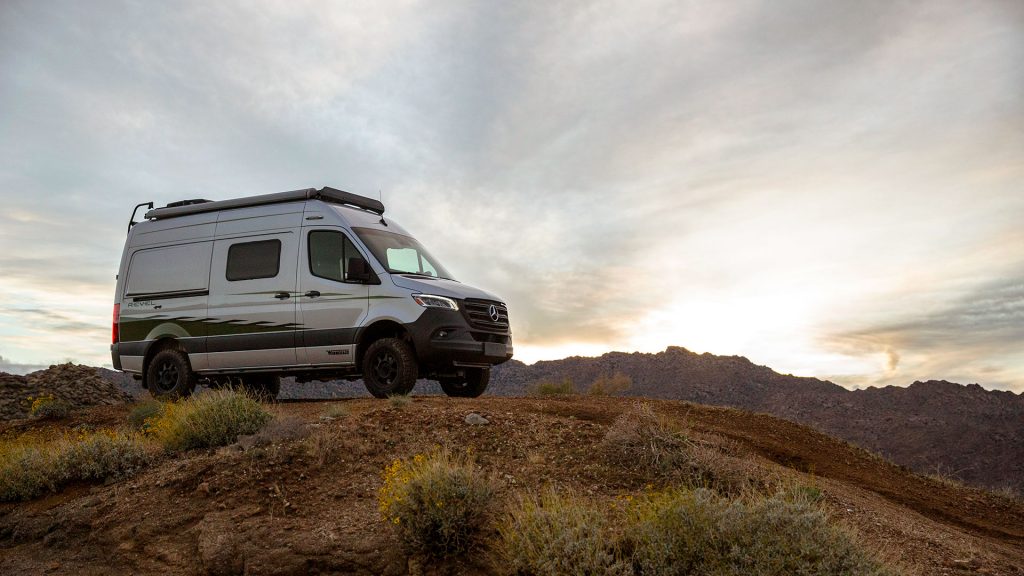 A silver Winnebago Revel RV sits atop a hill on at dusk. 
