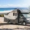 A black and white RV sits on a shore line with the awning deployed on a sunny day.