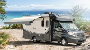 A black and white RV sits on a shore line with the awning deployed on a sunny day.
