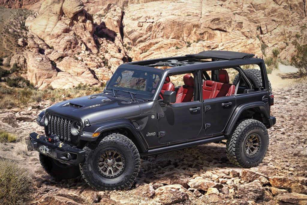 A black Jeep Wrangler with red interior sit at the base of rocky terrain with the tops off.