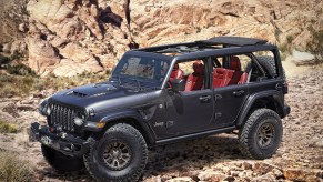 A black Jeep Wrangler with red interior sit at the base of rocky terrain with the tops off.
