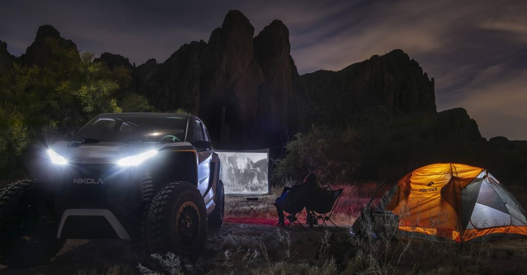 The electric NZT sits by a campsite with a makeshift screen in the background. The screen has a movie projected on it.