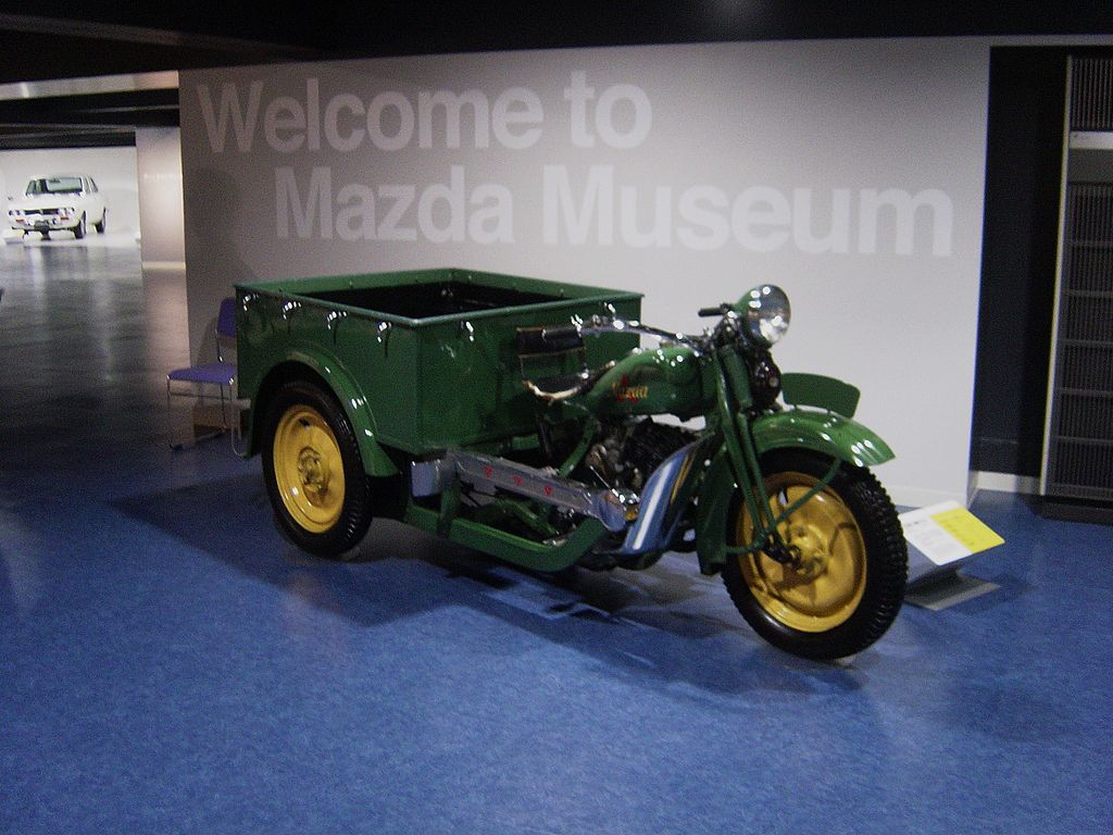 a green and yellow Mazda-Go tricycle truck on display at a museum