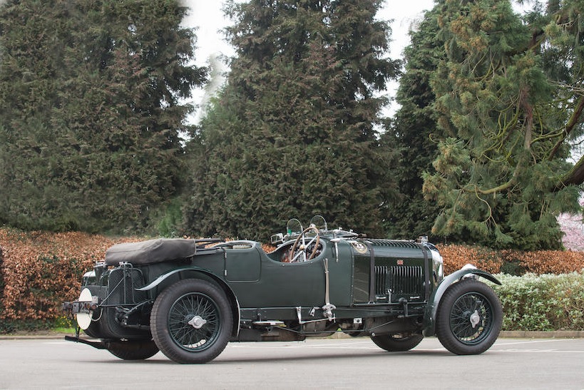 The rear-side view of a 1931 Supercharged 4 1/2 Litre Bentley in front of some pine trees