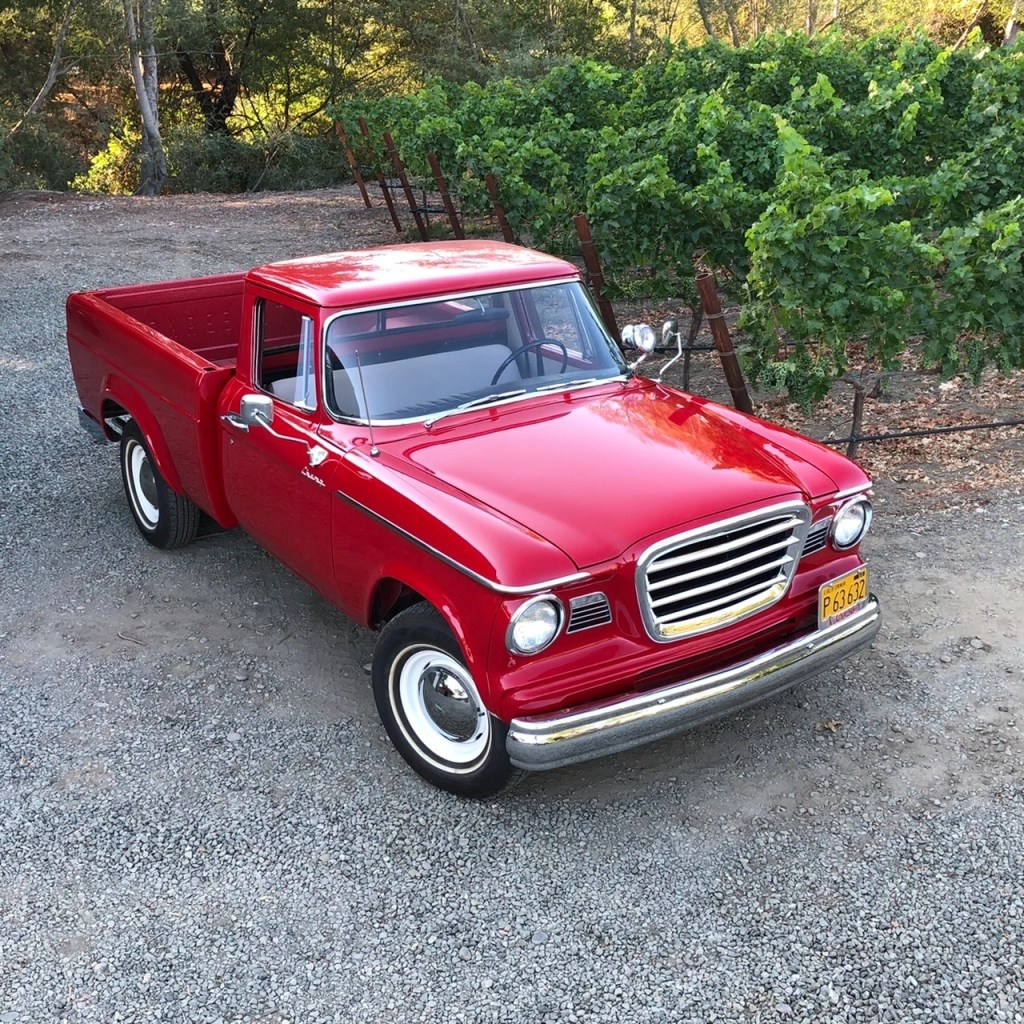 A red 1962 Studebaker Champ on a gravel driveway next to some bushes