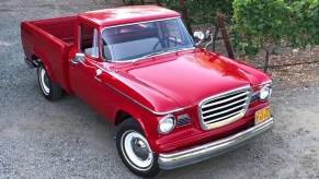A red 1962 Studebaker Champ on a gravel driveway next to some bushes