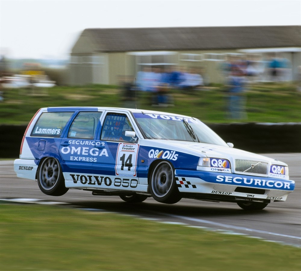 A white-and-blue 1994 Volvo 850 Estate BTCC racer goes up on 2 wheels on a racetrack corner