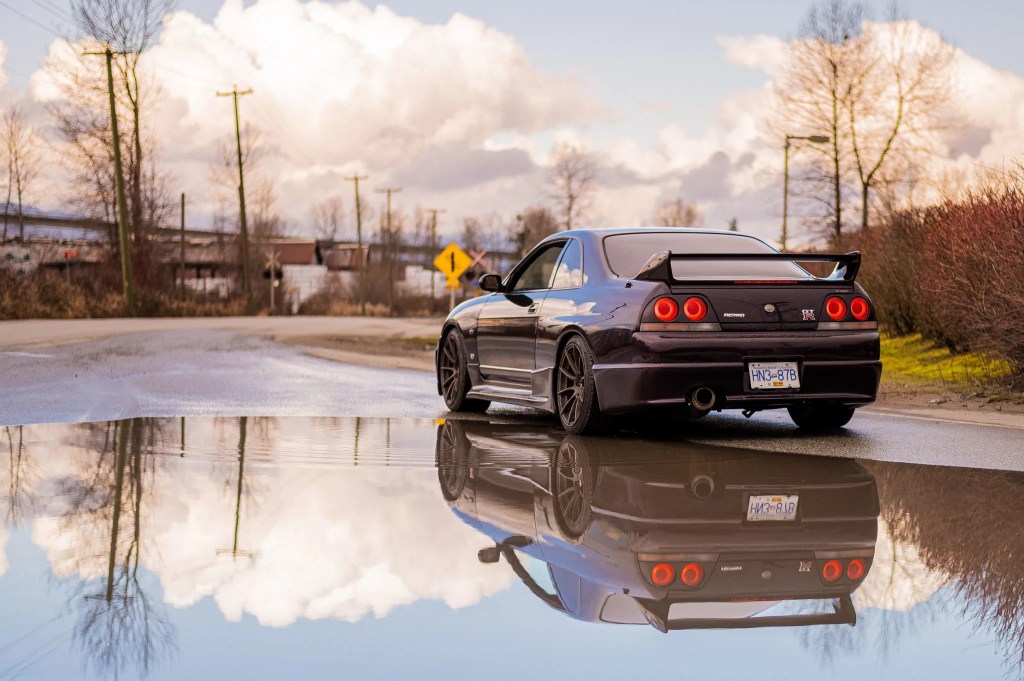 The rear view of a purple 1995 R33 Nissan Skyline GTR V-Spec in front of a puddle