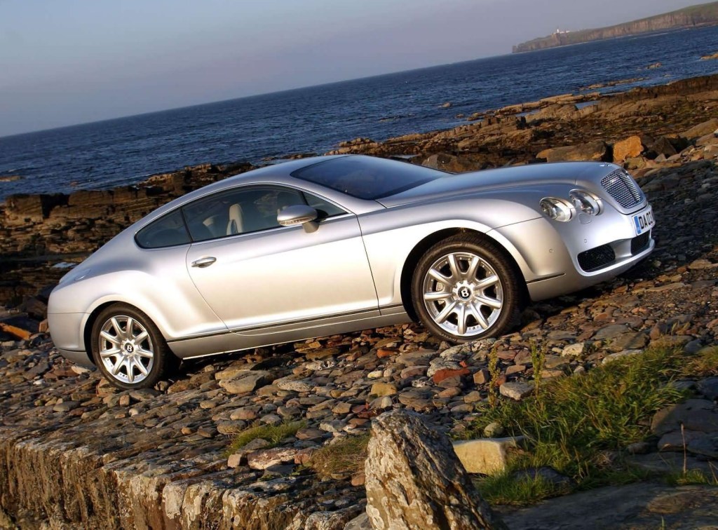 The side view of a silver 2003 Bentley Continental GT parked on a rocky beach