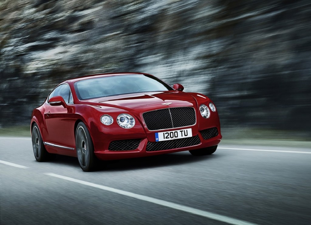 A red 2013 Bentley Continental GT V8 drives quickly down a forest road. This model made the most unreliable cars to avoid list and has potentially high repair costs. 