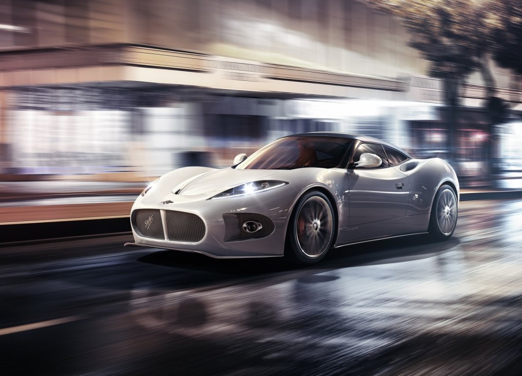 A white 2013 Spyker B6 Venator Concept drives through a brightly-lit city at night