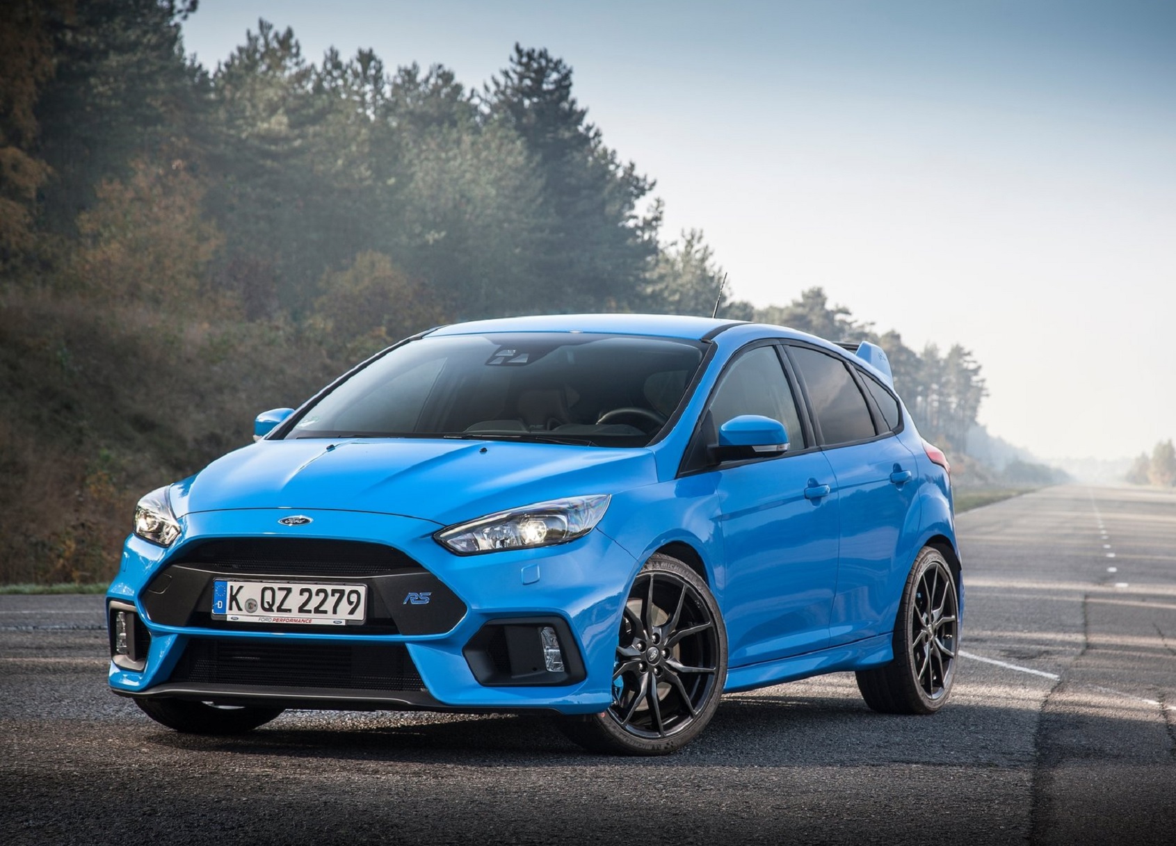 A blue 2016 Ford Focus RS on a tree-lined misty road