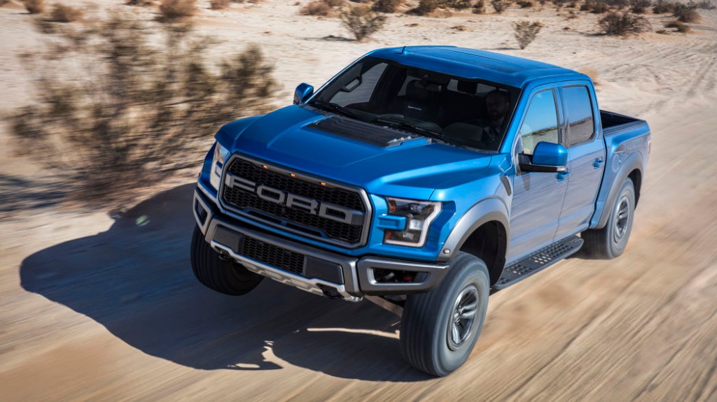 A blue 2019 Ford Raptor is powering through on a dirt road.